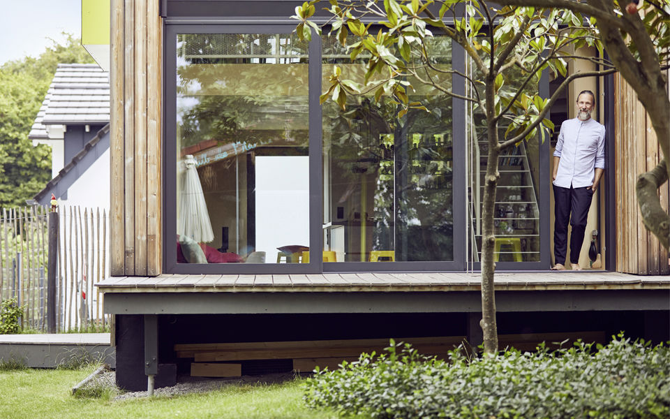 Mann steht in seinem Eigenheim und schaut glücklich aus dem Fenster.