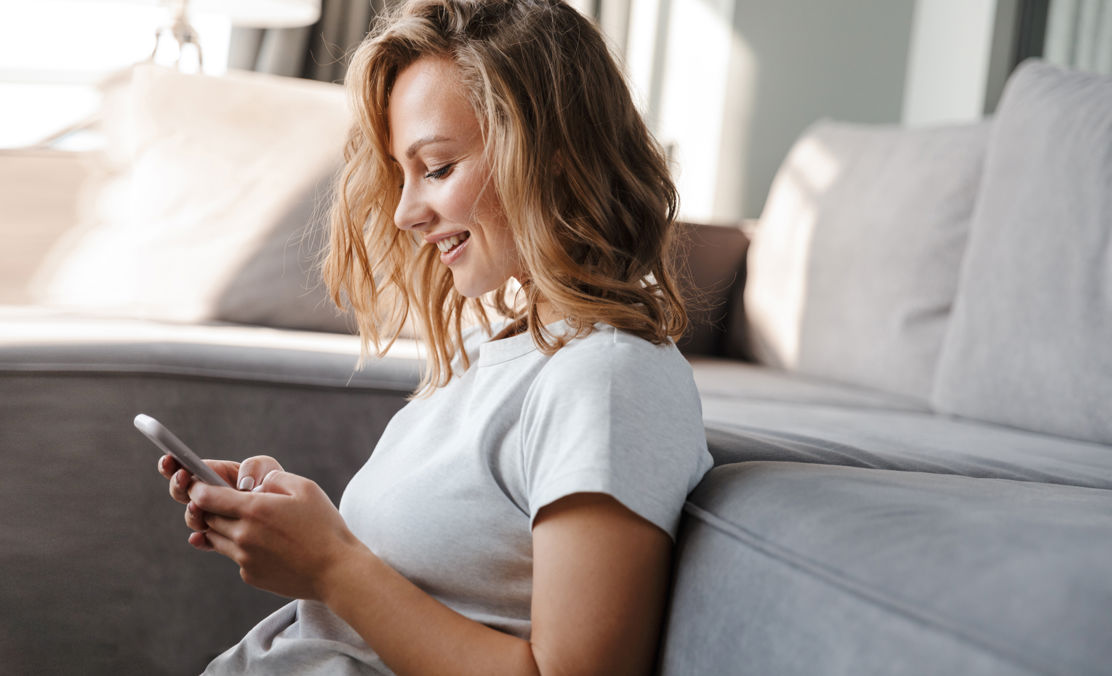 Das Bild zeigt eine Frau, die auf dem Boden sitzt und ein Smartphone in der Hand hält.