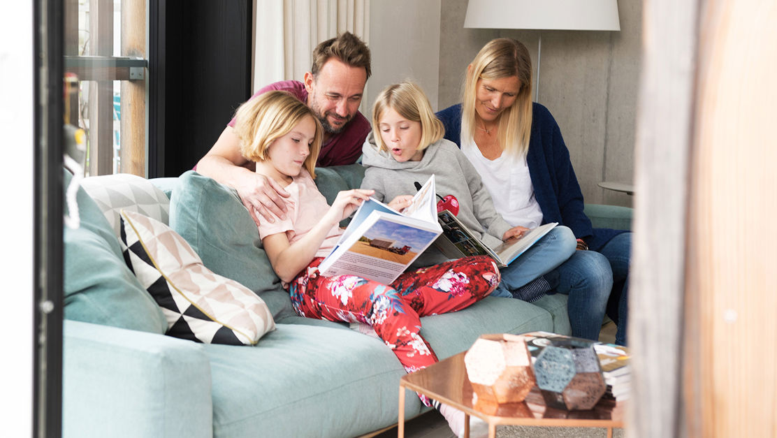 Familie sitzt im Eigenheim auf dem Sofa und fühlt sich abgesichert dank kollektiv Todesfallversicherung.