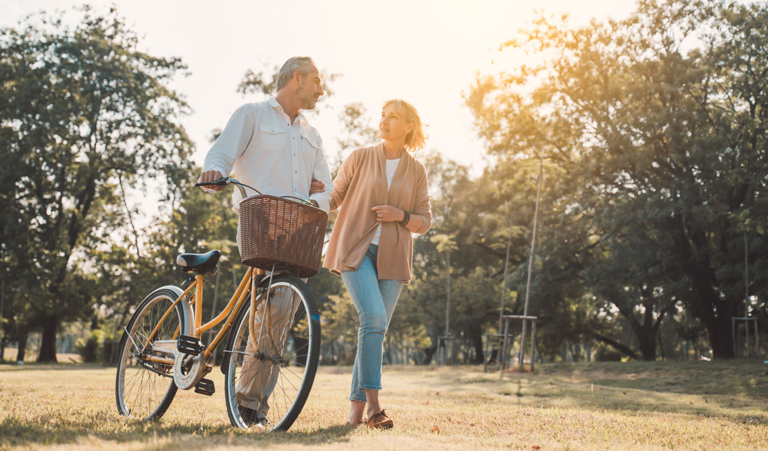 Paar bespricht den Inhalt der Beratung rund um die Pensionierung und stösst dabei das Fahrrad durch den Park.