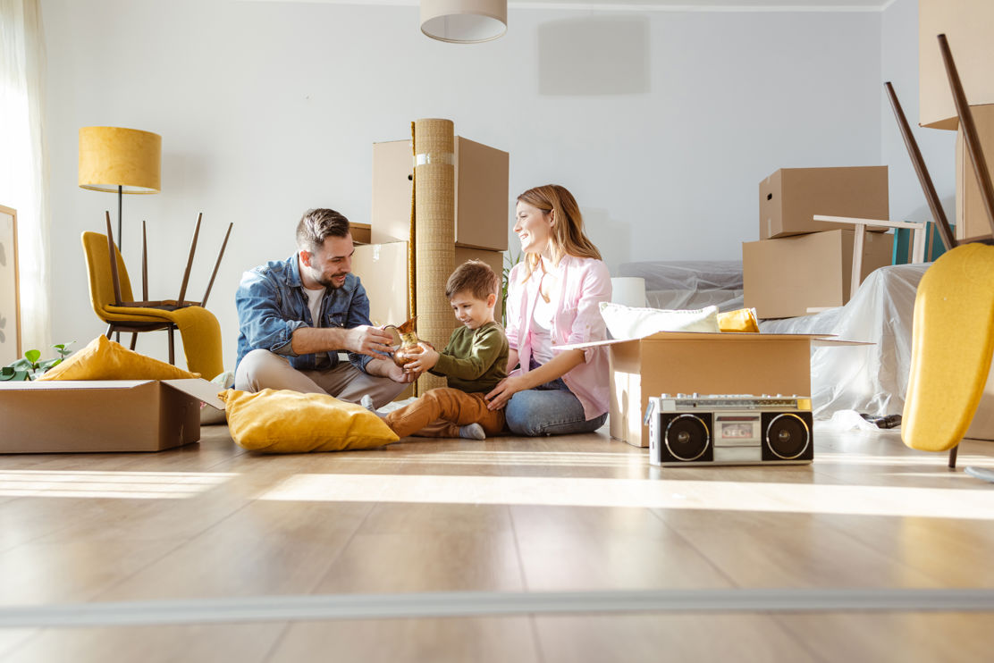 Junge Familie auf dem Boden ihres neuen Eigenheims, umgeben von Kartonschachteln