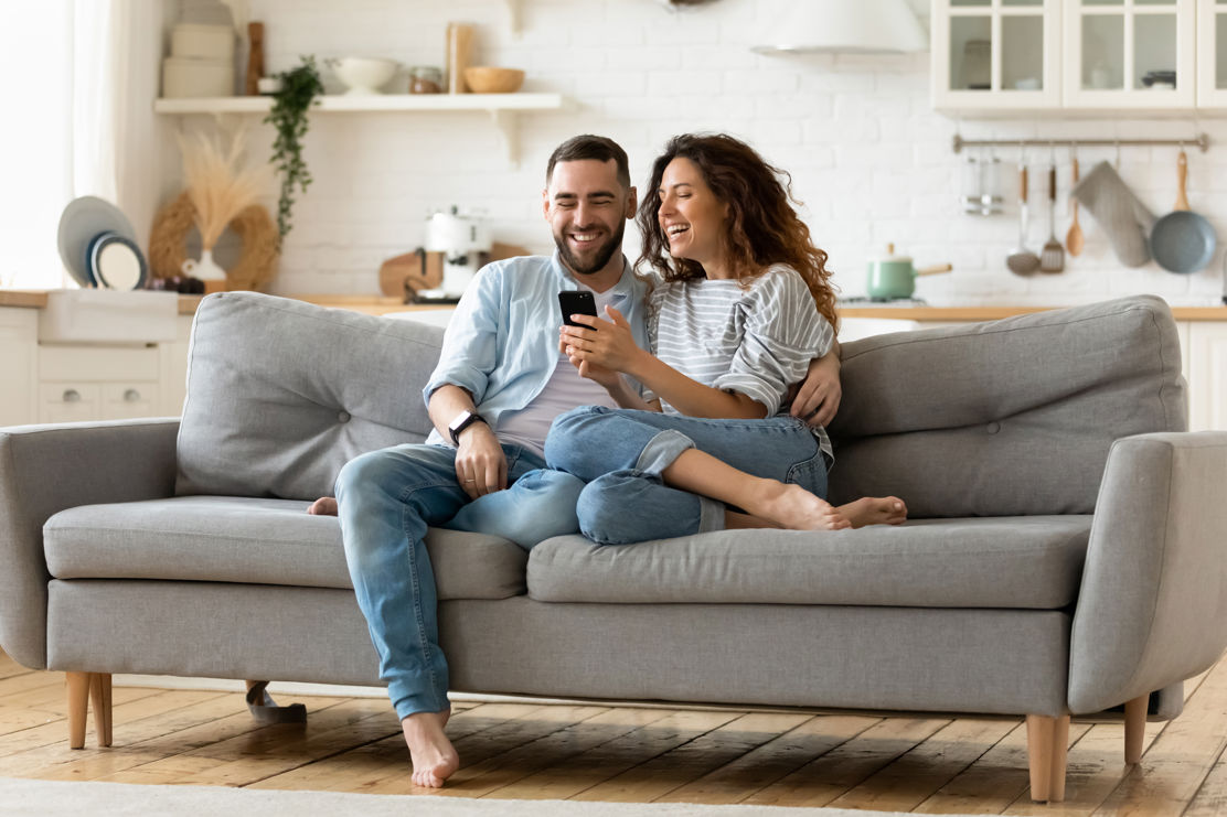 Paar sitzt mit dem Smartphone auf dem Sofa und plant ihre Altersvorsorge.