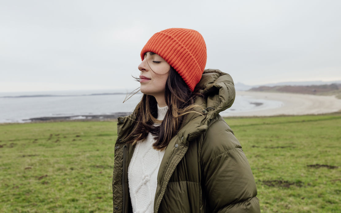 Junge Frau mit Mütze fühlt sich im Sabbatical an der Küste frei von finanziellen Sorgen, da sie weiss, wie sie ihr Sabbatical finanziert und ihre Altersvorsorge sicherstellt.