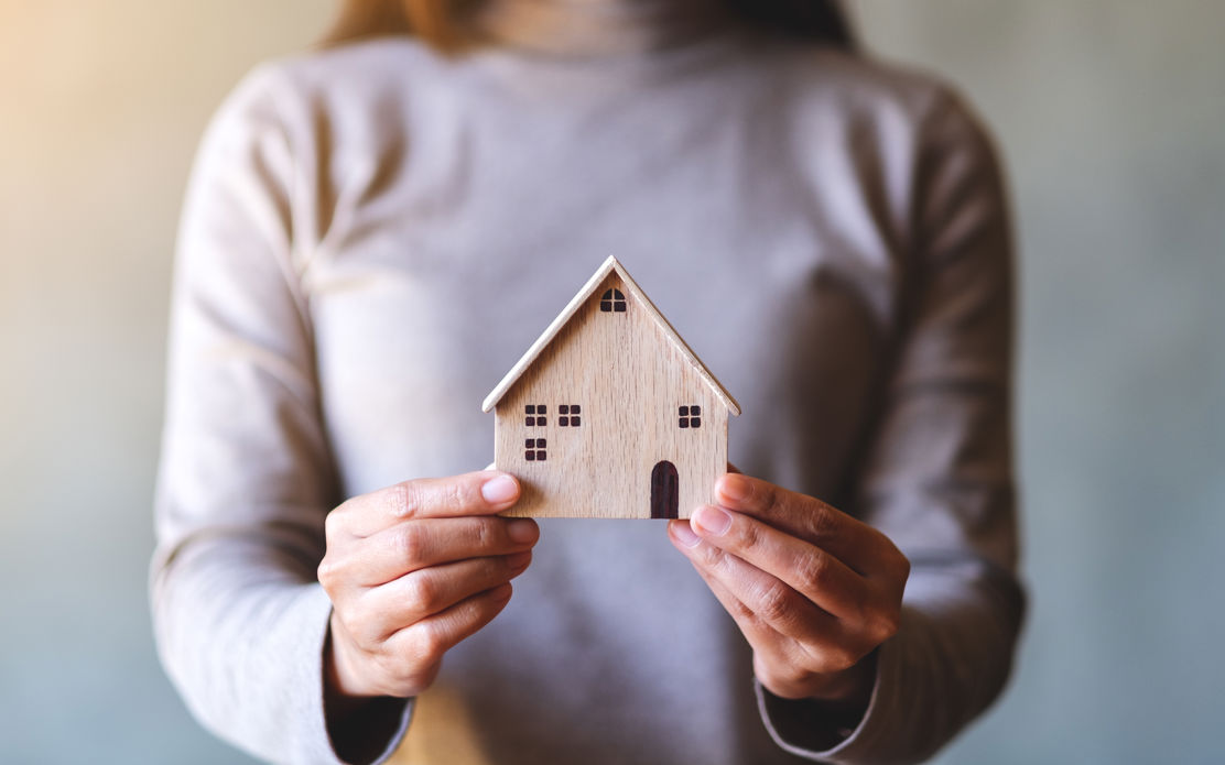 Frau, die ein kleines Modellhaus in der Hand hält und sich fragt, ob sie sich ein Eigenheim leisten kann.